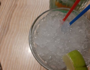 Masanın üzerinde bir bardak buzlu ve pipetli Mojito kokteyli var. Bu Küba içeceği taze nane, limon ve rom, buz içeriyor..