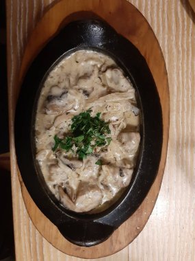 Tahtada domuz eti, mantar ve soğanlı oval siyah bir tava var..