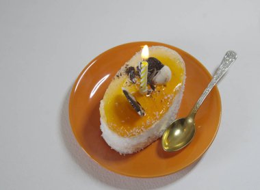 Beyaz arka planda, portakallı seramik bir fincan çay, bir fincan kek ve yanan bir mum..