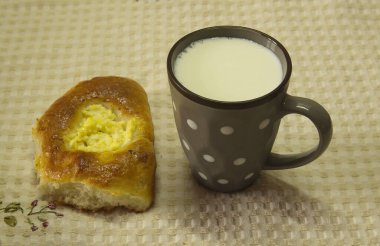 On a beige tablecloth there is a gray ceramic cup with milk and homemade cakes: fresh curd cheesecakes.