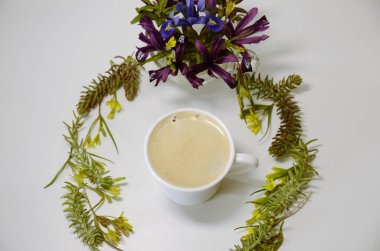 Beyaz arka planda, bir fincan kahve ve taze bahar çiçekleri ile bir kompozisyon..