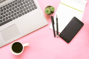 Bilgisayarlı pembe ofis masası, akıllı telefon, defter, kahve ve kaktüs. Üst görünüm