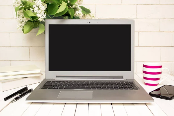 Laptop, akıllı telefon, kitaplar, kahve ve çiçekli modern ofis masası.