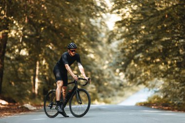 Bisiklet, kask ve gözlük giymiş sportif vücut şekli olan olgun bir sporcu yaz ormanında bisikletle ayakta duruyor. Sakallı adam spor yaparken temiz havanın tadını çıkarıyor..