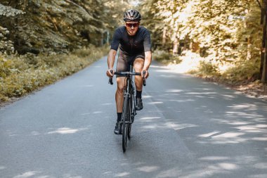 Spor giysili, koruyucu kasklı ve aynalı gözlüklü mutlu olgun bir adam yaz ormanlarında bisiklet sürüyor. Profesyonel bisikletçi düzenli olarak temiz hava alıyor..