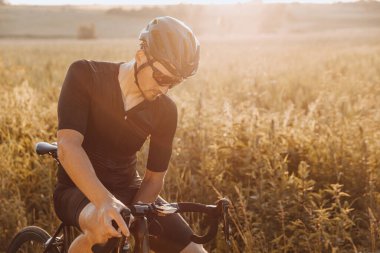Aktif giyimli, siyah kasklı ve spor gözlüklü profesyonel bisikletçi doğada bisiklet sürmeye ara veriyor. Dışarıda antrenmandan sonra yorgun adam dinleniyor..