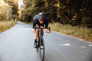 Koruyucu kasklı ve aynalı gözlüklü sakallı adam daha hızlı gidebilmek için yarı eğimli bir şekilde bisiklete biniyor. Aktif giyinen profesyonel sporcu yarışlara hazırlanıyor..