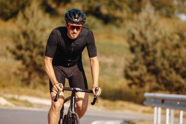 Spor kıyafetli, koruyucu kasklı ve aynalı gözlüklü güçlü erkek sporcu yeşil arka planda bisiklet eğitimi alıyor. Etkin ve sağlıklı yaşam tarzını kavra.