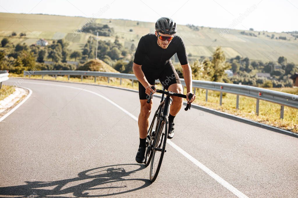 Athletic bearded man in active clothing, black helmet and mirrored glasses riding black bike with background of beautiful nature. Concept of activity and sport.