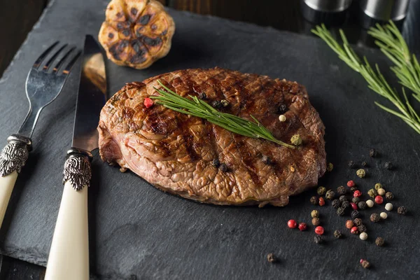 Steak de bœuf grillé sur plaque de pierre sur table en bois avec fourchette et couteau . — Photo