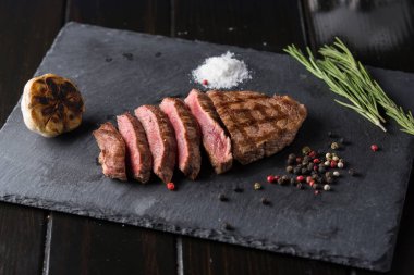 Başbakan antrikot biftek siyah taş tabağa dilimlenmiş. Biftek doneness orta düzeyde. Biberiye ve biber ile. Çatal ve bıçak.