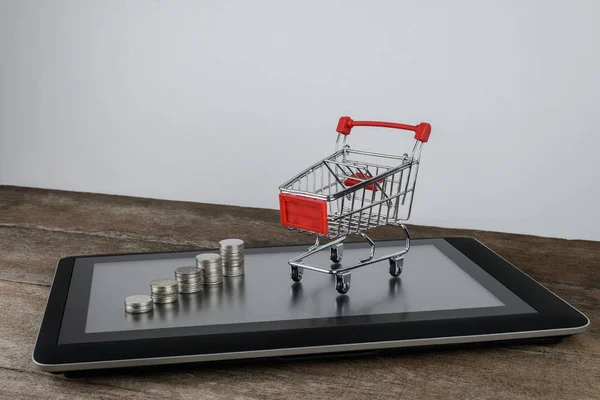 Shopping cart and coin stacks on tablet — Stock Photo, Image