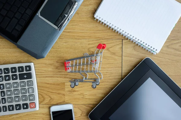 Kleine rode shopping cart, trolley en gadgets op tafel — Stockfoto