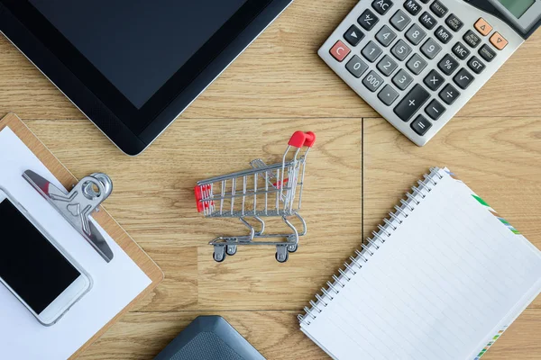 Kleine rode shopping cart, trolley en gadgets op tafel — Stockfoto