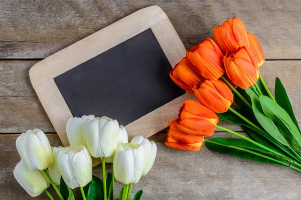 Colorful tulips bouquet and chalkboard on wooden background — Stock Photo, Image