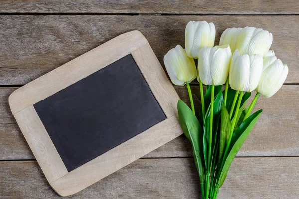 Colorful tulips bouquet and chalkboard on wooden background — Stock Photo, Image