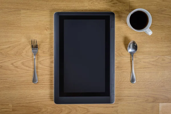 Tableta sobre mesa de madera con cuchara, tenedor y taza de café — Foto de Stock