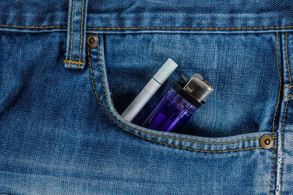 Сигареты и дешевая зажигалка в старом джинсовом кармане — стоковое фото