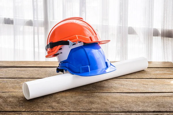 蓝色坚硬安全帽建筑帽子为技工的安全项目作为工程师或工作者 工程学建筑工作者设备以蓝图 在木地板 窗口光和窗帘是背景 — 图库照片