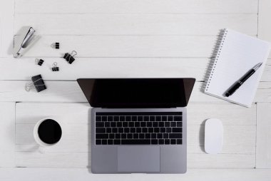 Düz yatıyordu, ahşap ofis masasının üstünde. Not defteri, fare bilgisayarı, dizüstü bilgisayarı, akıllı telefon, kalem, ataç, zımba, kahve fincanı ofis malzemeleri beyaz ahşap arka planda coppy alanı olan çalışma alanı