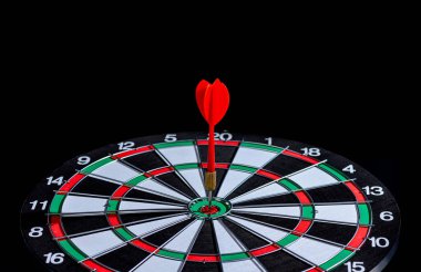 Kara zemin üzerinde hedef merkezindeki Dart tahtasına isabet eden kırmızı dart oku hedefe ulaşma kavramını belirliyor iş hedeflerine meydan okuyor ve hedefe ve pazarlama kavramına ulaşmaya hazır.