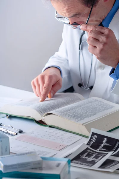 Старший Доктор шукає інформацію в медичній книзі — стокове фото