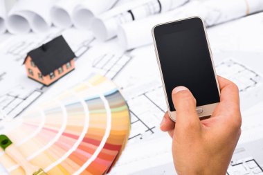 Bir akıllı telefon inşaat planları üzerinde tutan erkek el