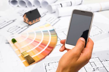 Bir akıllı telefon inşaat planları üzerinde tutan erkek el