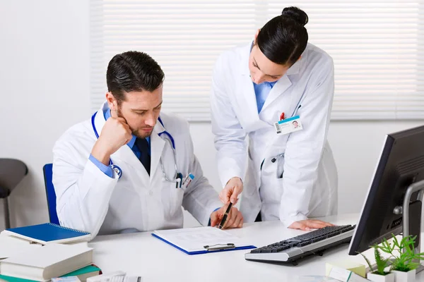 Δύο γιατροί συζητώντας ασθενής σημειώσεις σε ένα γραφείο — Φωτογραφία Αρχείου
