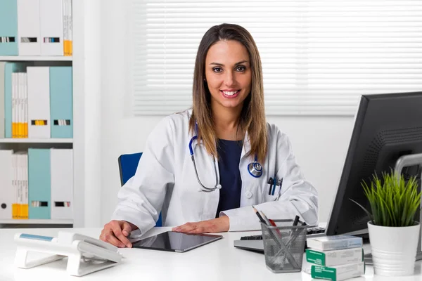 Усміхнена жінка-лікар за столом за допомогою планшета — стокове фото