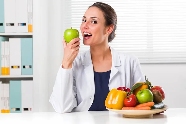 Женщина-диетолог ест зеленое яблоко в своем офисе — стоковое фото