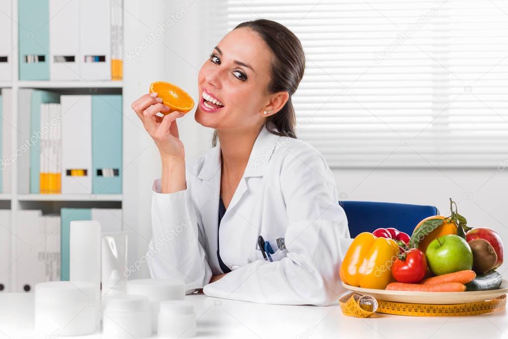 Female nutritionist eating an Orange Slice in her office