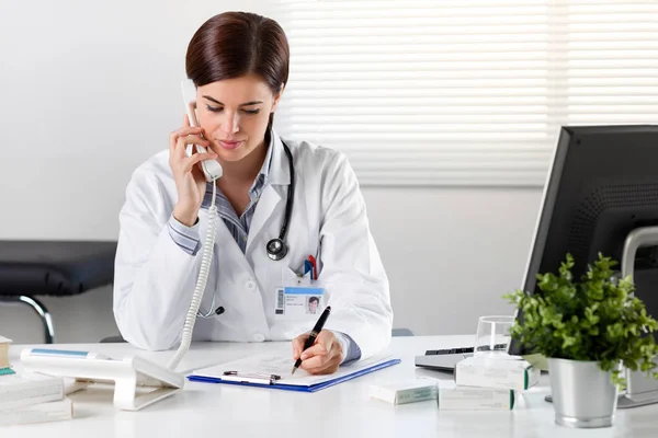 Жінка-лікар за столом з телефоном — стокове фото
