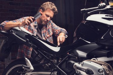 Bir atölyede klasik bir motosiklet üzerinde çalışan bir adam.