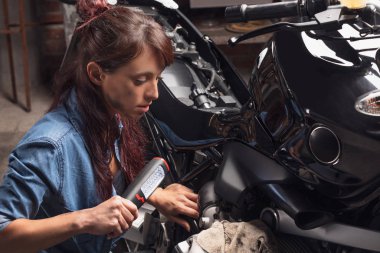 Klasik bir motosiklette çalışan genç bir kadın.