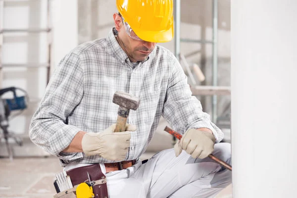 Construtor ajoelhado usando um cinzel e martelo — Fotografia de Stock