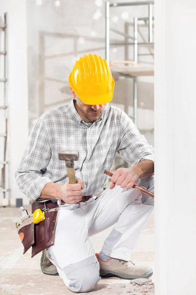 Construtor ajoelhado usando um cinzel e martelo — Fotografia de Stock