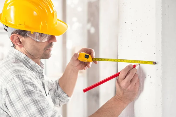 Builder marking measurements on a white wall