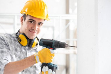 Young construction worker drilling wall indoors
