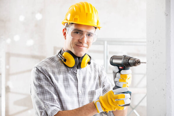 Young construction worker drilling wall indoors