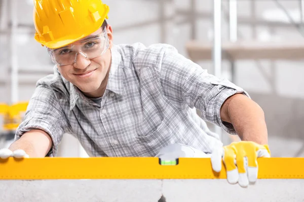 Construtor sorridente em um chapéu duro usando um nível de espírito — Fotografia de Stock