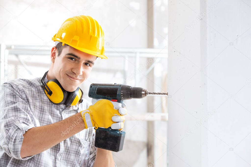 Young construction worker drilling wall indoors