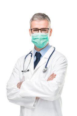 Doktor, enfeksiyonlara karşı cerrahi maske takıyor. Kolları çapraz duran, beyaz önlüklü, Corona virüsü ya da Covid-19 konseptinde izole edilmiş bir laboratuvar önlüğü giyiyor.