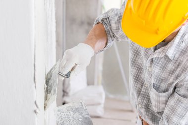 Su sızıntısı veya nem nedeniyle oluşan nemli bir bölgenin onarımı sırasında beyaz bir duvara alçı eklemek için mala kullanan bir inşaat işçisi