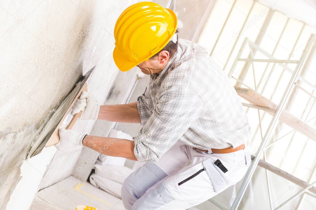 Builder applying new plaster to a wall indoors covering a damp stain during renovations and repairs in a high key close up image