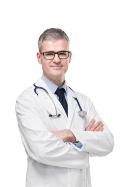 Beyaz önlüklü, gözlüklü ve steteskoplu kendine güvenen erkek doktor kollarını kavuşturmuş beyaz tenli kameraya gülümsüyor.