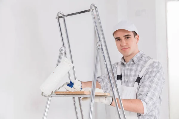 Amigável Jovem Pintor Decorador Macacão Boné Branco Inclinado Uma Escada — Fotografia de Stock