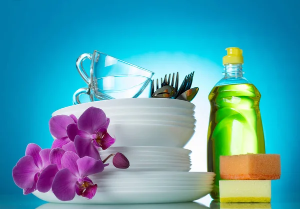 Clean washed dishes and cutlery on blue background, a branch of an orchid