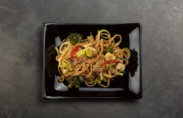 Piatto nero con tagliatelle aromatiche cinesi su tavolo scuro — Foto Stock