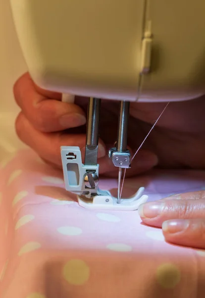 Macro. Manos femeninas en la máquina de coser eléctrica blanca tela rosa con lunares — Foto de Stock